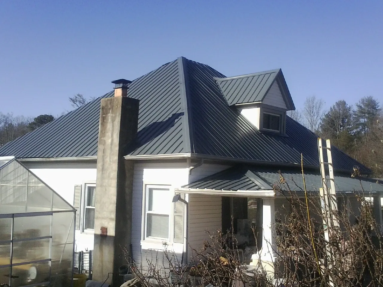 Dark blue standing seam metal roof on a white farmhouse with dormer — Slate & Tile Roof Repair by Roofing Brothers in Palco