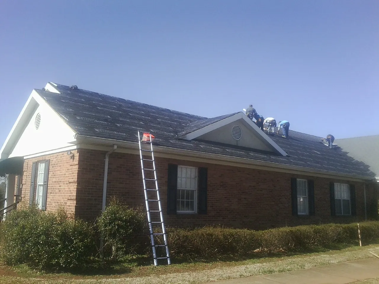 Crew tearing shingles off a brick ranch roof with a ladder set — Emergency Roof Repair work by our crew in Palco