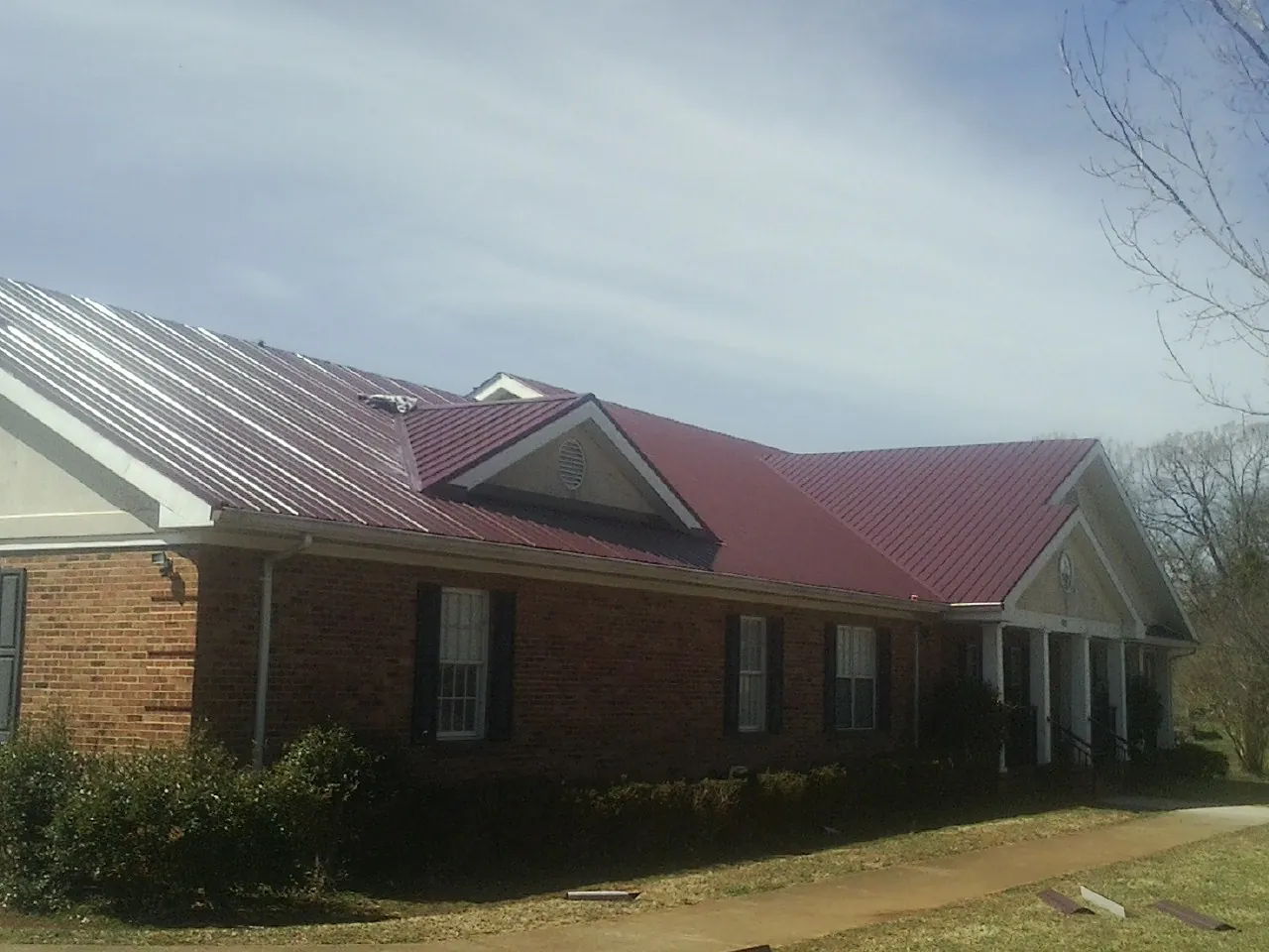 Red metal roof with gabled entries on a long brick building, from a Hail Damage Roof Repair job in Palco