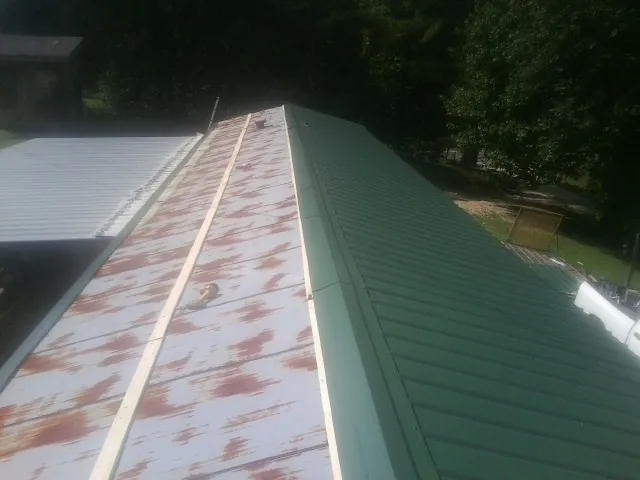 Old rusted panels beside newly installed green metal roofing — Wind Damage Roof Repair by Roofing Brothers in Palco