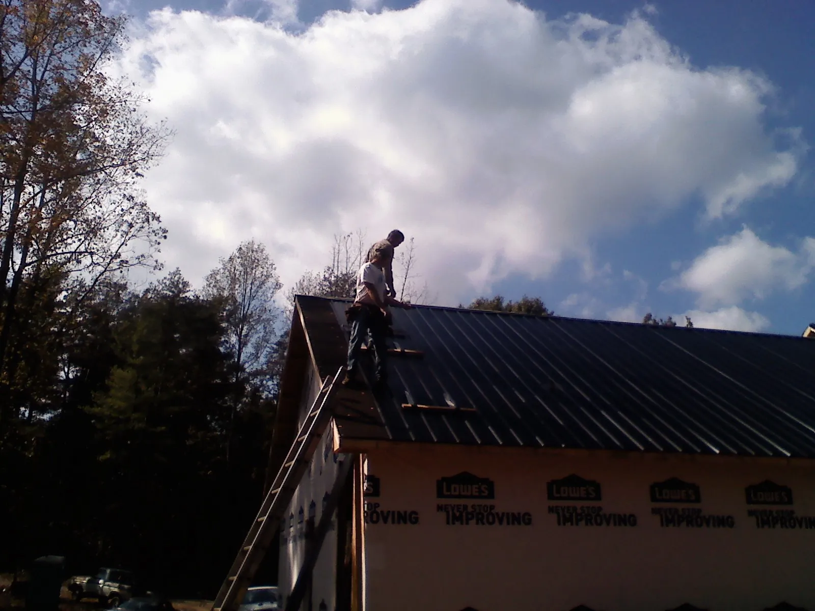 Roofer fastening dark metal panels high against a cloudy sky, from a Roof Inspection job in Palco