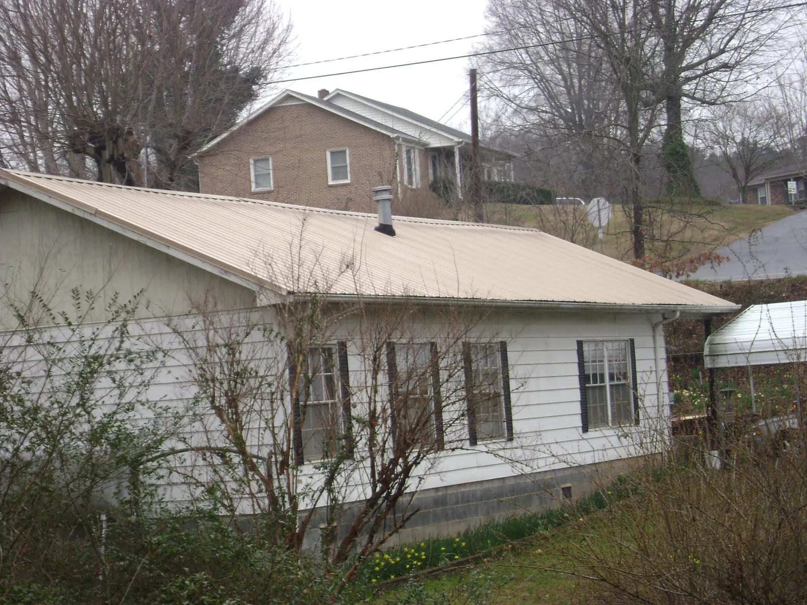 Tan metal roof on a white sided house set into a hillside — Commercial Roofing by Roofing Brothers in Palco