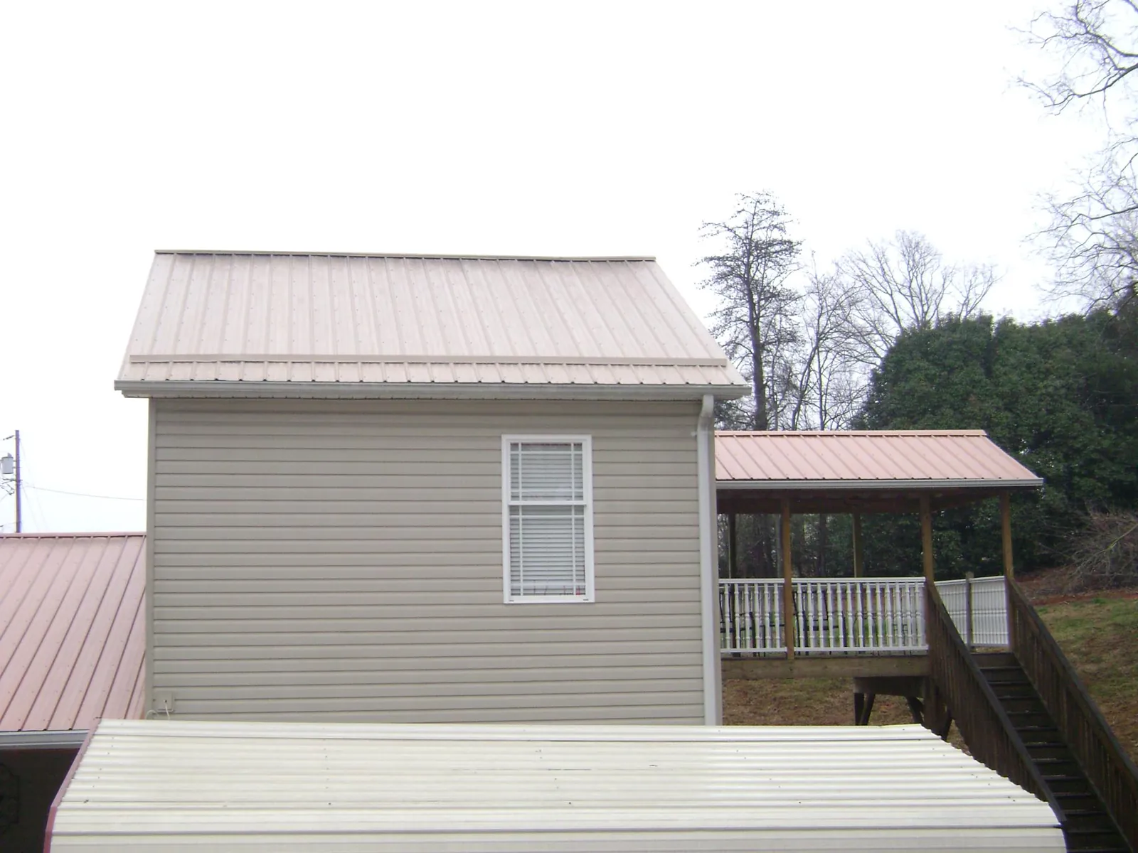 Tan metal roofs on a two story addition and attached porch, from a Roof Replacement job in Palco